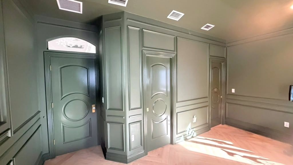 Wall paneling and trim with raised molding details, finished in a deep green satin across walls, doors, and casings.