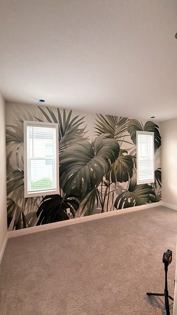 Large-scale tropical leaf mural installed across the main bedroom wall, with seams matched around both windows.