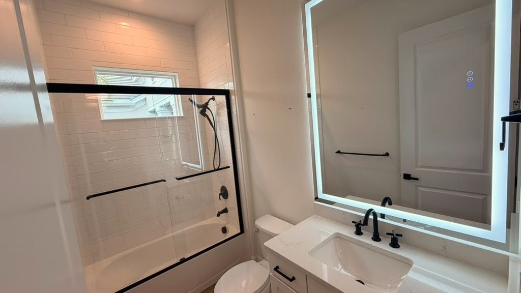 Shower tile surround with a framed glass door, new vanity, and a backlit mirror, finished with matching black fixtures.