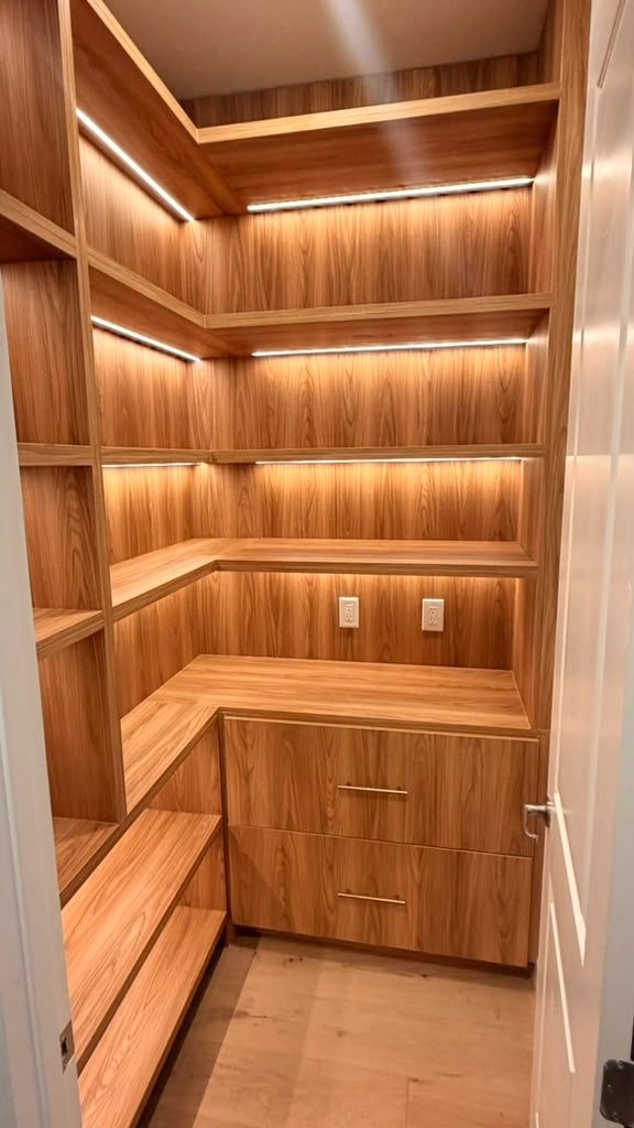 Custom walk-in closet with wraparound shelving, integrated LED strips, and a drawer bank finished in warm wood tones.