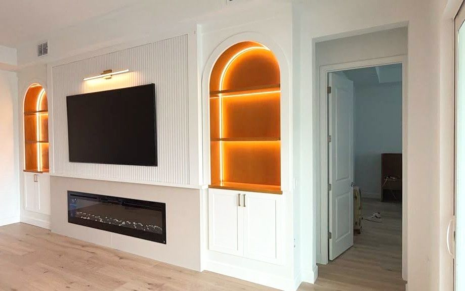 Built-in media wall with a linear electric fireplace, recessed TV, and lit arched niches on both sides.