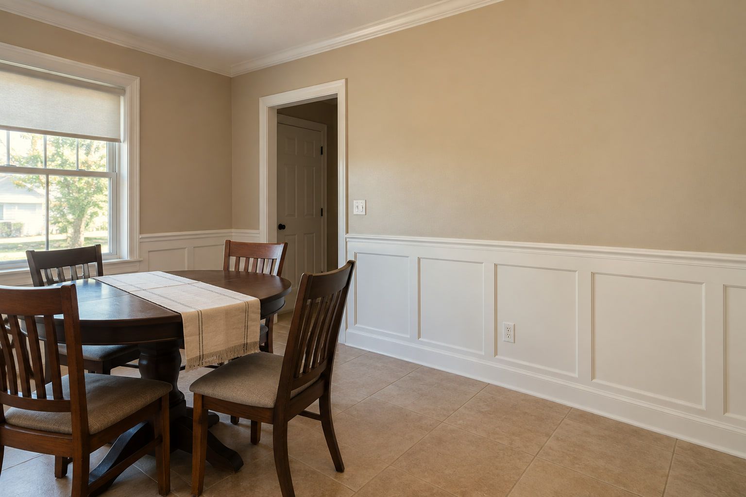 Dining room walls in a warm beige above white-painted wainscoting, with the crown, casings, and baseboards finished to match.