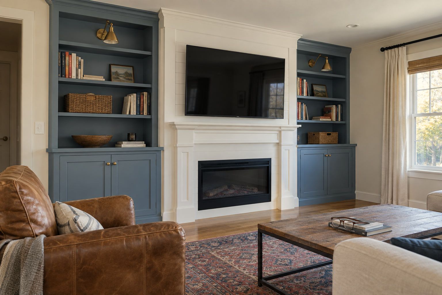 Painted built-in bookcases with cabinets and brass sconces on both sides of a white fireplace surround, with the TV mounted on shiplap above the mantel.